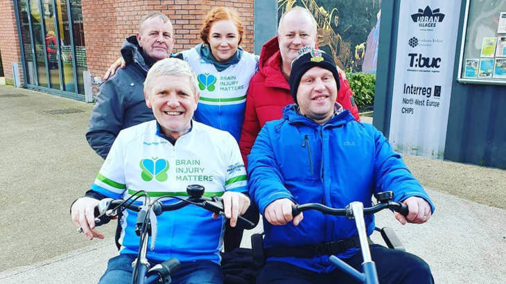 Graham Hill on Walk Wheel Cycle Trust’ side-by-side tandem bike at the Active Travel Hub in C.S. Lewis Square, Belfast. with Brain Injury Matters staff