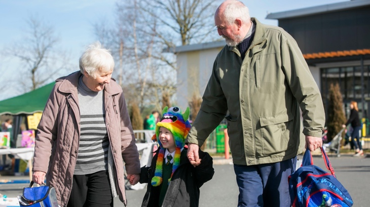 A pair of smiling grandparents pick up their grandchild from school