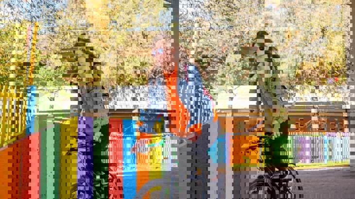 girl cycling past colourful fence