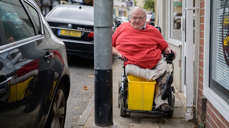 A man using a wheelchair navigating along a narrow pavement in Bristol