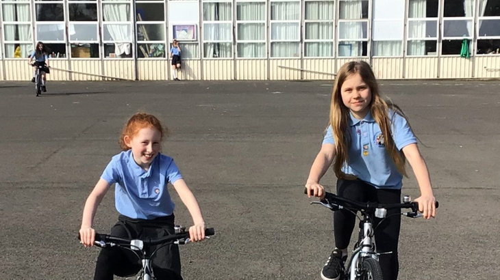 Two girls in school uniform on bikes in their playground