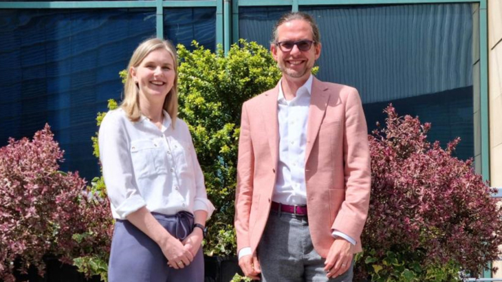 A blonde woman called Karen wearing a white shirt stood smiling next to a man called Xavier who is smiling and wearing a white shirt and a salmon blazer