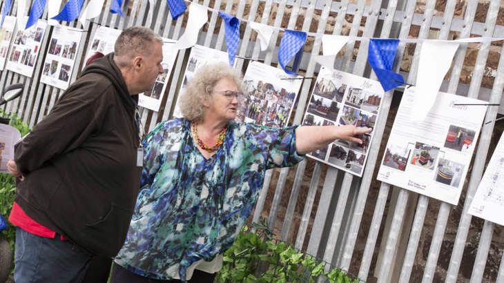 Two residents stand together discussing designs for their high street on big photography boards pinned to a railing