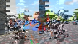 Children walking across a road while a woman pushes a buggy in the background