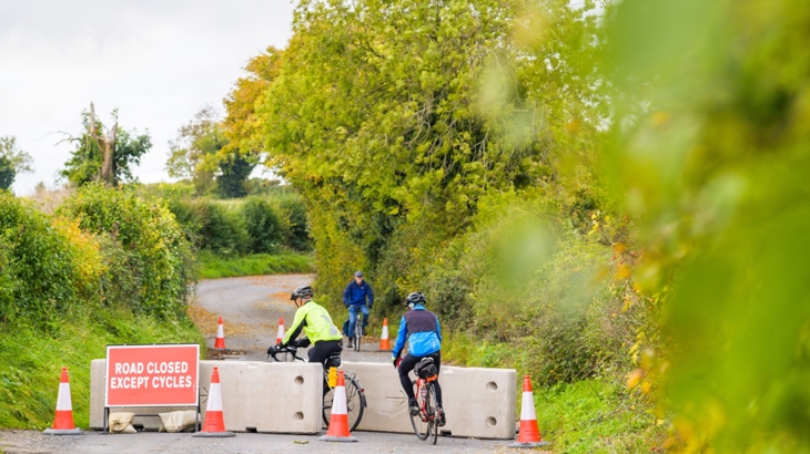 The temporary measures originally put in place on Chilton Road in Upton. Shows the temporary barriers with cyclists passing through them with a sign saying :Road closed except for cyclists. 