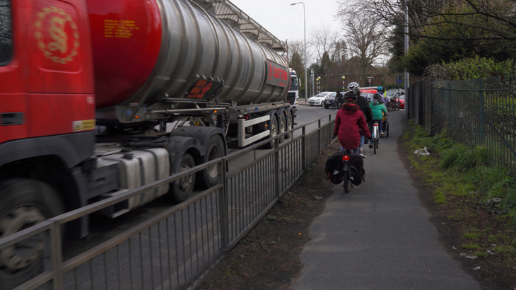 Kate and her children cycle on a shared-use pavement alongside a busy dual carriageway beside passing lorries.