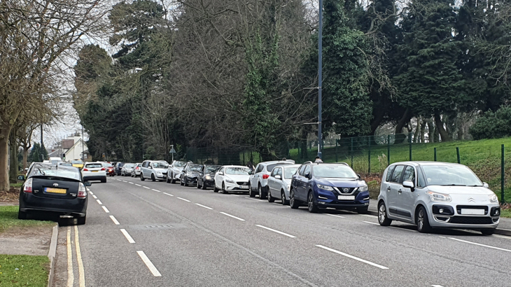 Lines of cars parked outside a school block cycle lanes on both sides of the road.