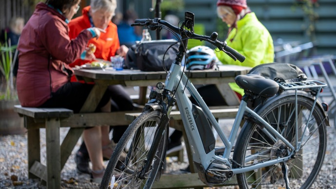 Three women sat at a picnic bench taking a break from an outdoor adventure with their electric bikes