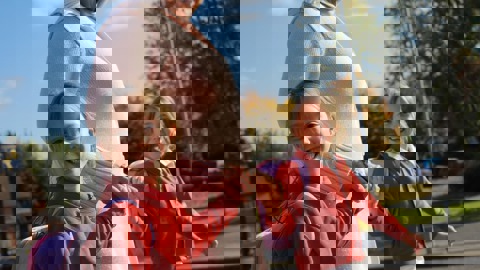 Mum walking to school, holding hands with her twin daughters smiling at the camera