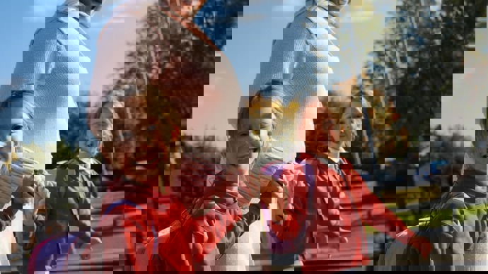 Mum walking to school, holding hands with her twin daughters smiling at the camera