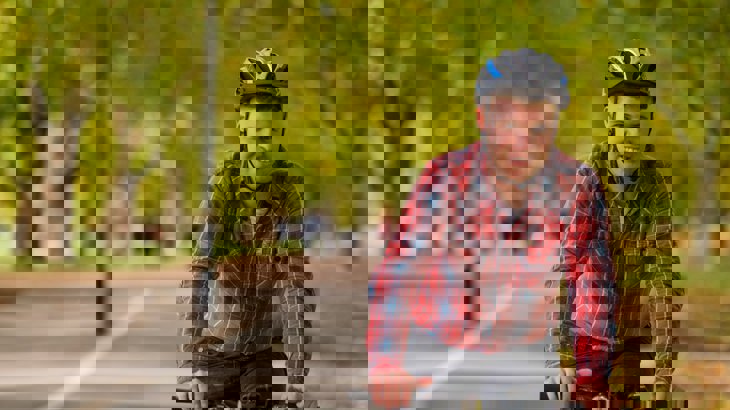 Man in red shirt and cycling helmet riding on cycle path through wooded park