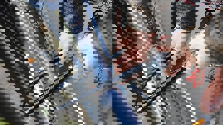 Person's hands locking blue bike frame to black railings using black D-lock