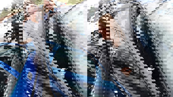 Three women chat outside of a car in a car park 