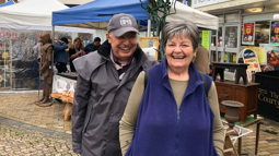 An older man and woman stood next to each other in a town both smiling