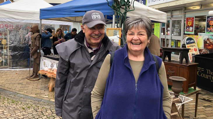 An older man and woman stood next to each other in a town both smiling