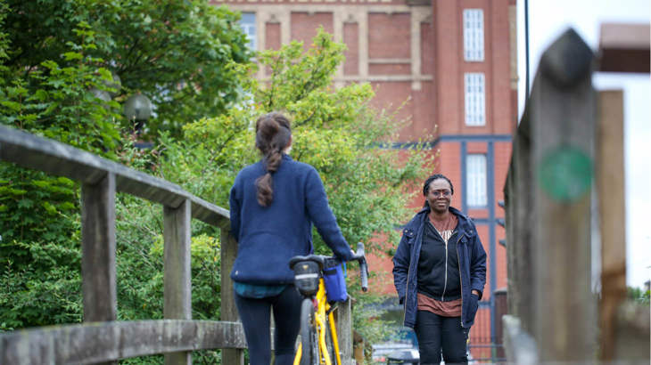 A person walking across a bridge in Manchester city, with someone walking past them pushing a bicycle.