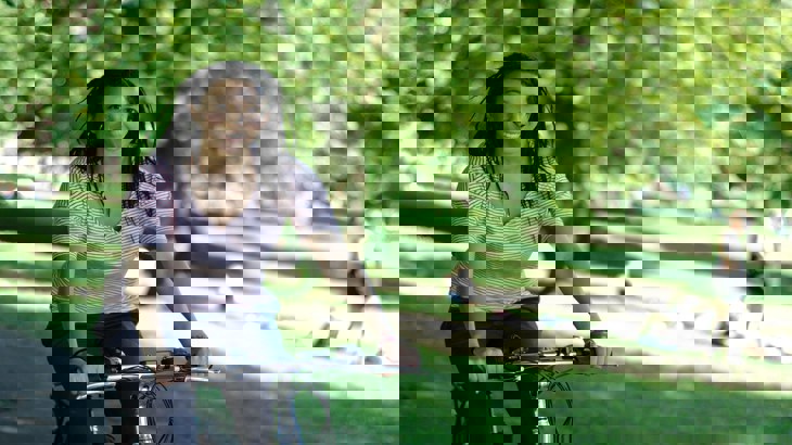 Lady smiling riding her bike through sunny park 