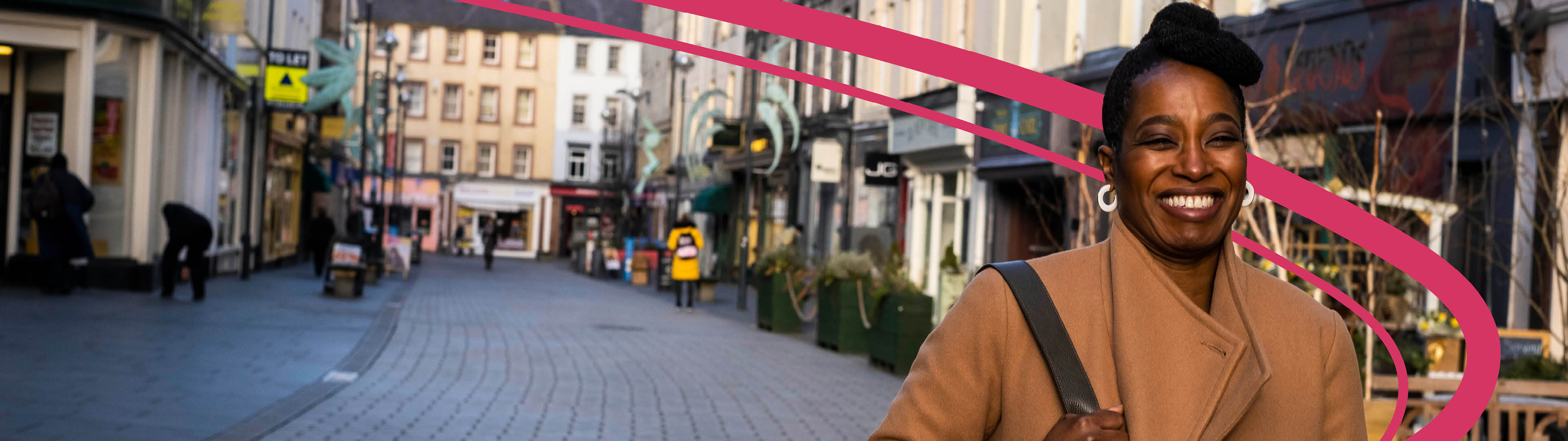 Woman smiling and walking down a pedestrianised high street.