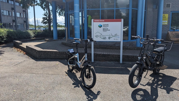 Two e-bikes positioned in front of Natural Resources Wales' Rivers House office.