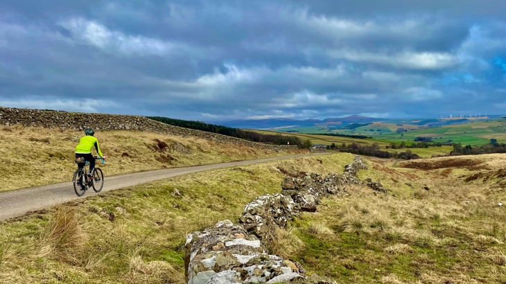 A lone person cycles across the brow of a hill in Glenkiln, looking out to wide open landscapes and down to Glenkiln Reservoir.