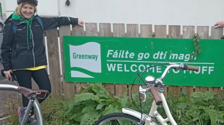 A woman wearing a helmet stands beside a fence and two bicycles.