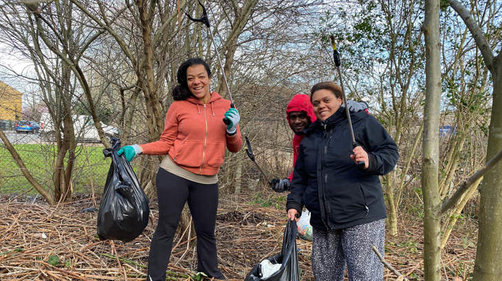 Two volunteers holding litterpickers and bags smiling, surrounded by autumnal trees.
