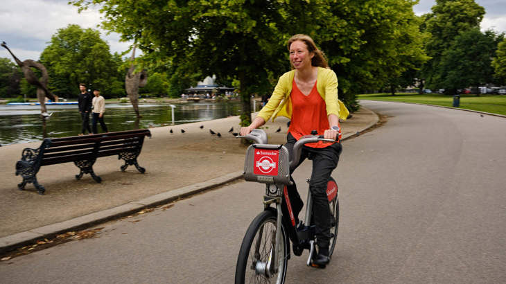 Woman cycling on a Santander bike through Victoria Park in Hackney, London.