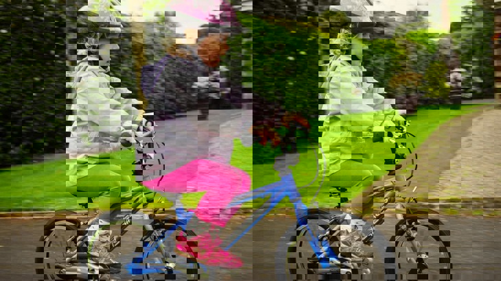 Little girl in pink helmet cycling past on a blue bicycle