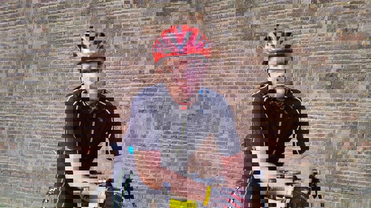 Man in black cycling top and red cycling helmet leaning on road bike handlebars 