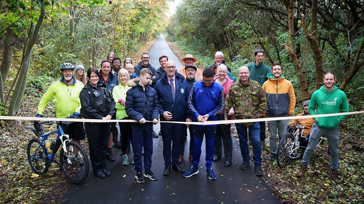a boy with scissors is about to cut a ribbon on a cycle route, next to a group of people smiling