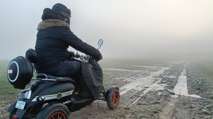 A man on a mobility scooter wrapped in warm clothing on an off-road track on a misty day in England