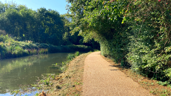 newly resurfaced and improved towpath runs next to canal, and trees line both sides.