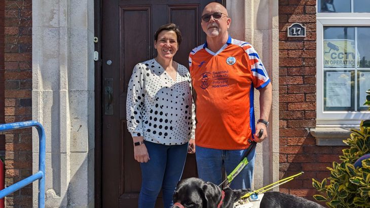 Mark Evans, a registered blind person, meets his MP Tonia Antoniazzi in Swansea. They stand together outside her office with Mark's guide dog, Bobby.