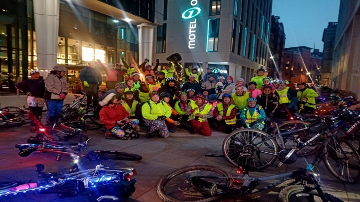 a group of women with lots of creative lights on their bikes at night, next to a statue