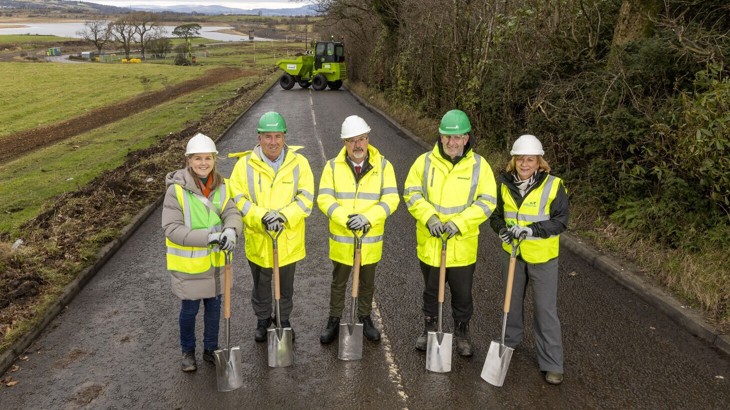 The project partners all gathered in high visibility jackets smiling to camera and ready for the start of construction of the path.