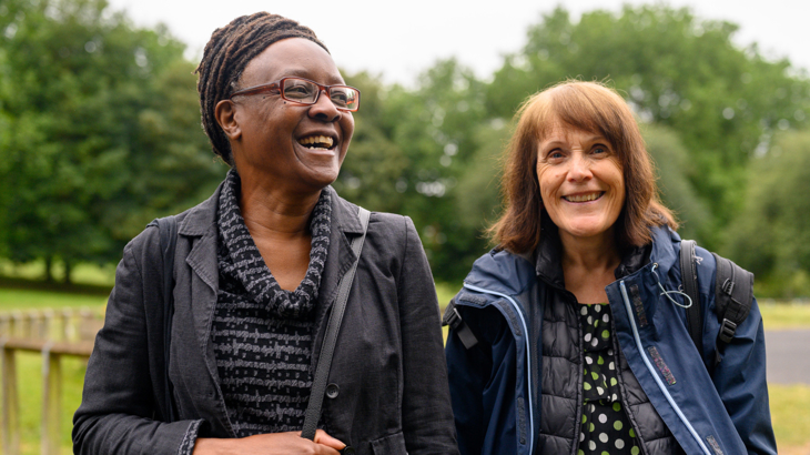 Two older women stood next to each other outside smiling on an overcast day