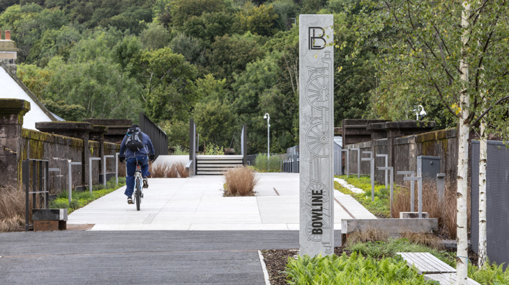 A person cycles off into the distance on a newly made bridge over Bowling Harbour, near Dumbarton on National Route 7, with greenery in the background
