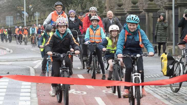 A group of schoolchildren on bikes using a dedicated cycle route with adults trailing behind.