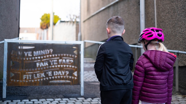 Two children look at a decorative metal barrier featuring phrases in the Caithness dialect that has been installed in Wick.