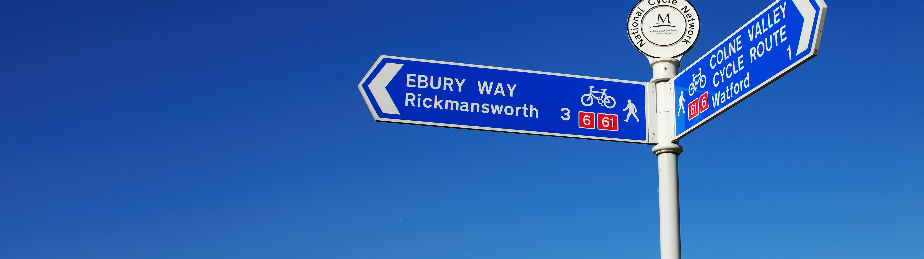 National Cycle Network Route sign pointing left in front of a clear blue sky. The sign directs route 6 and route 61.