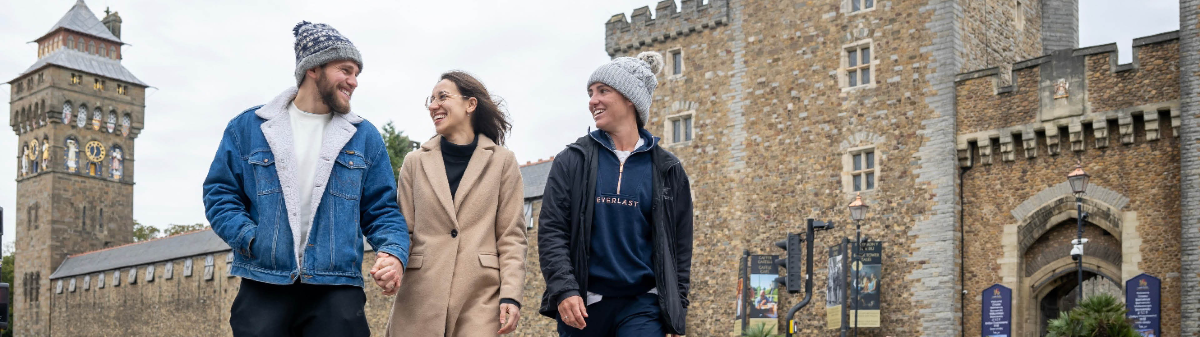 Three young people walking on Castle Street in Cardiff, with the castle in the background.