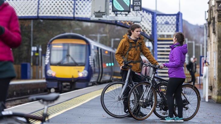 A group of people wait on a railway platform with bicycles.
