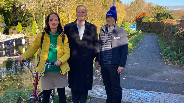 Three people stood on a National Cycle Network path on a sunny day with a Network sign in the background