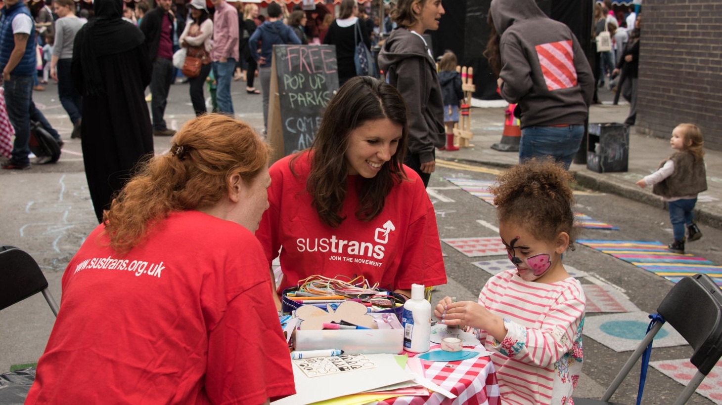 Two volunteers sitting at a table doing crafts with a little girl