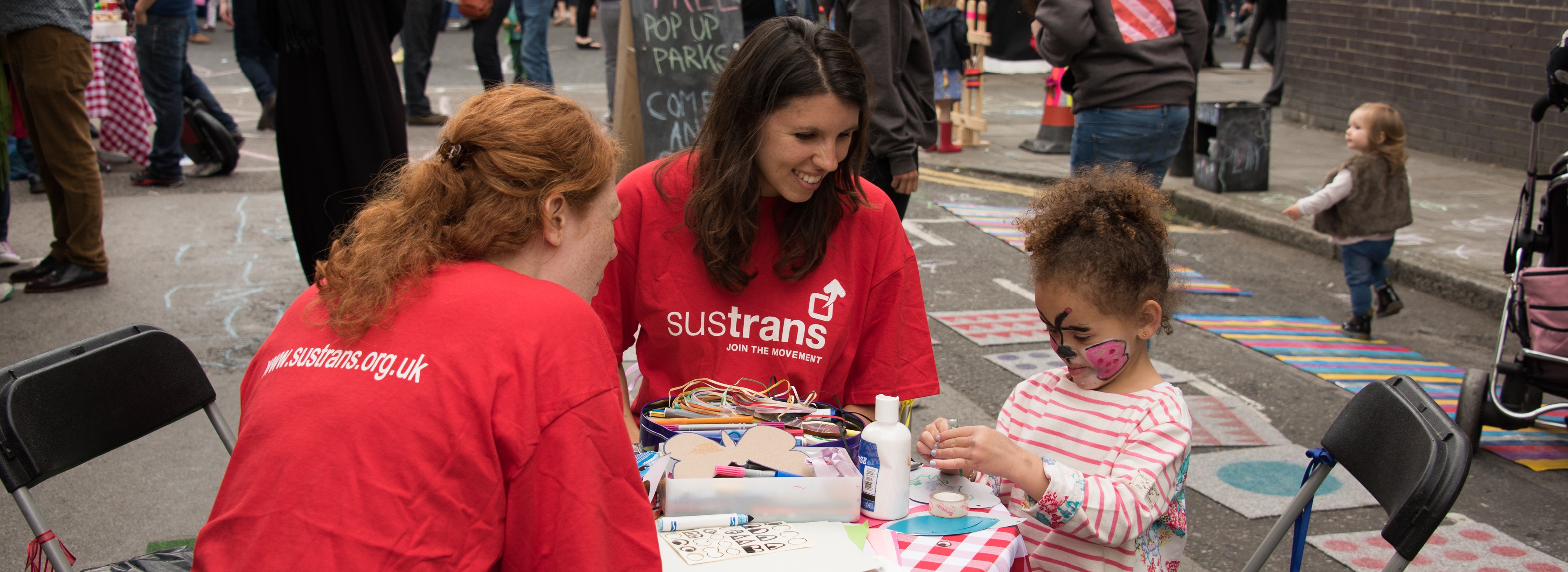 Two volunteers sitting at a table doing crafts with a little girl in London