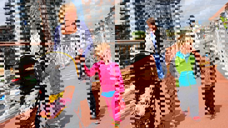 Woman with baby in pushchair with two small children and older woman, walking over bridge in urban area