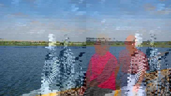 Older man and woman sitting on stone wall by reservoir with bike leaning