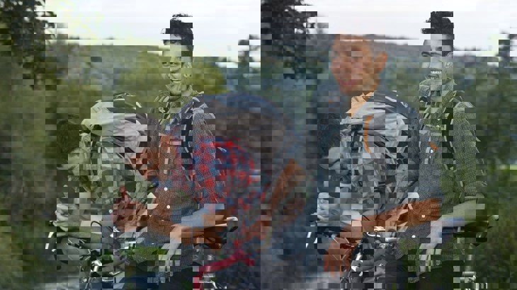 Two men wearing backpacks, resting on their bikes