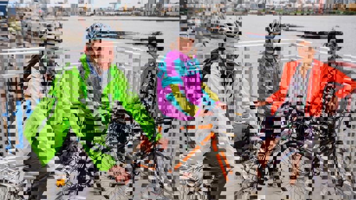 Three cyclists in brightly-coloured jackets, two of them wearing helmets, by the Thames in London