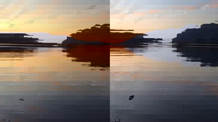 View of flat-calm lake reflecting pink and blue sky and hills